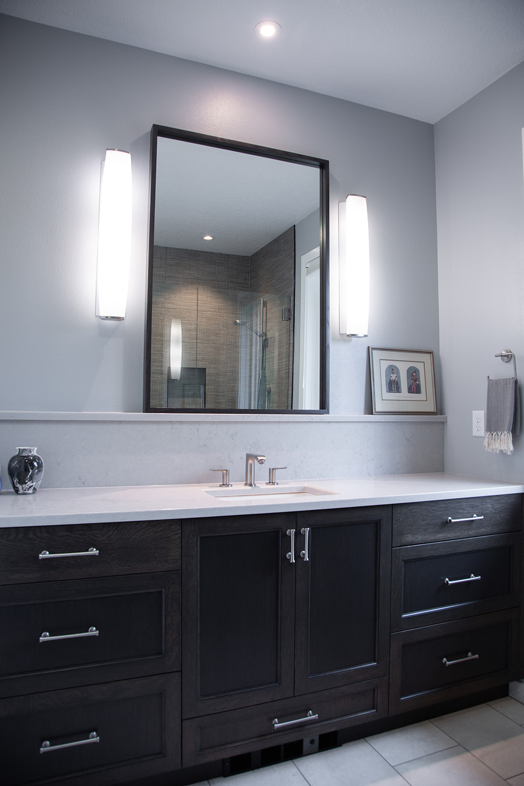 guest bath vanity with dark stained cabinets and quartz countertop, wall sconces with framed mirror