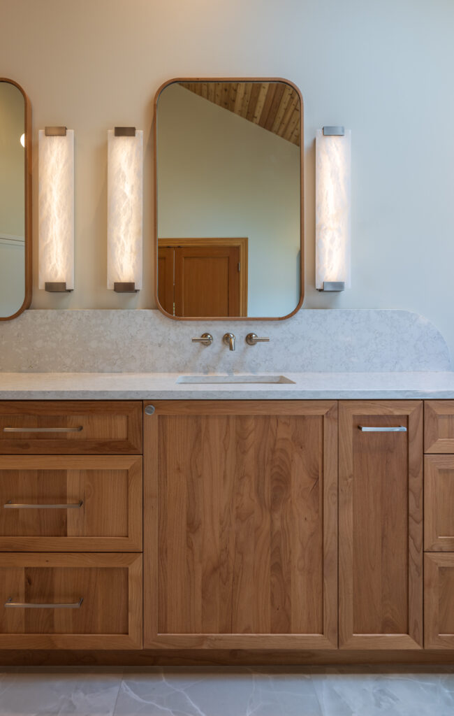 Large, double vanity with quartz counters and alabaster sconces, wall mounted faucets, in satin nickel finish, custom wood framed mirrors with rounded edges, and custom curved backsplash.