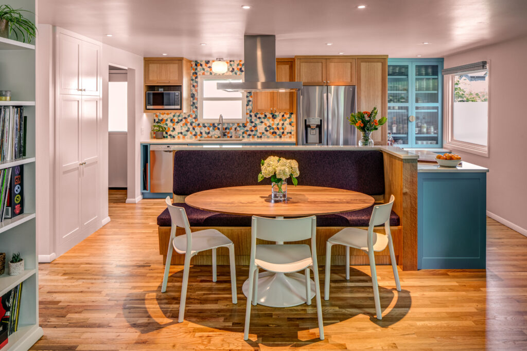Kitchen with blue and wood cabinets, banquette seating, dining table, mosaic backsplash