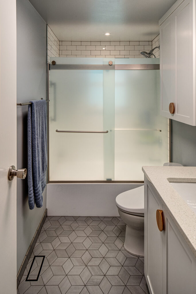 Bathroom with custom vanity, subway tile, toilet topper, sliding shower door, geometric mosaic floor tile