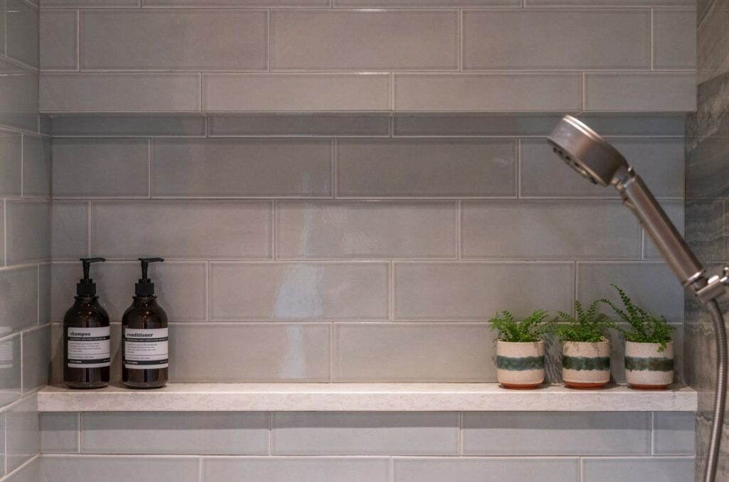 Shower niche with potted plants, shampoo and conditioner, quartz ledge and tile walls.